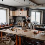 Artists collaborating in a shared woodworking workshop with tools and a laptop