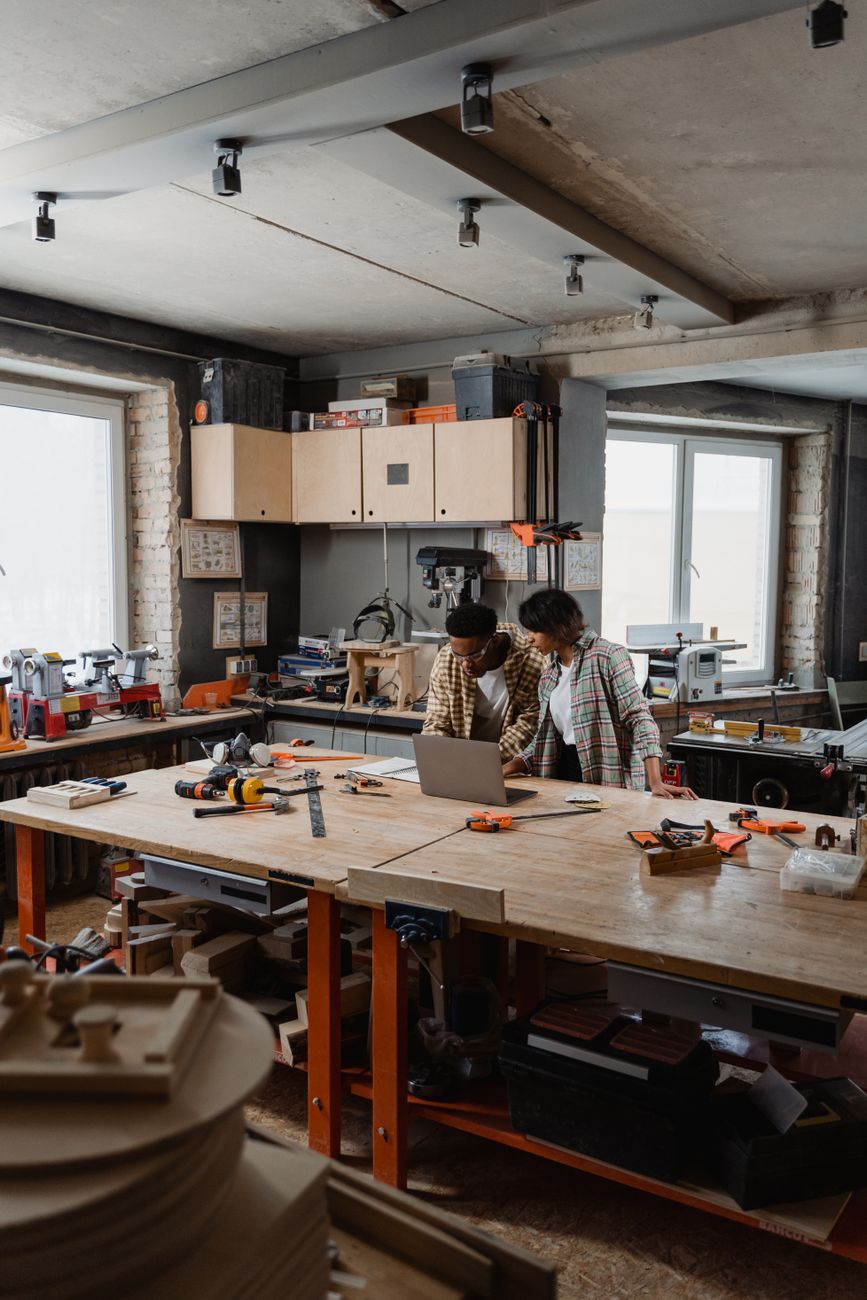 Artists collaborating in a shared woodworking workshop with tools and a laptop